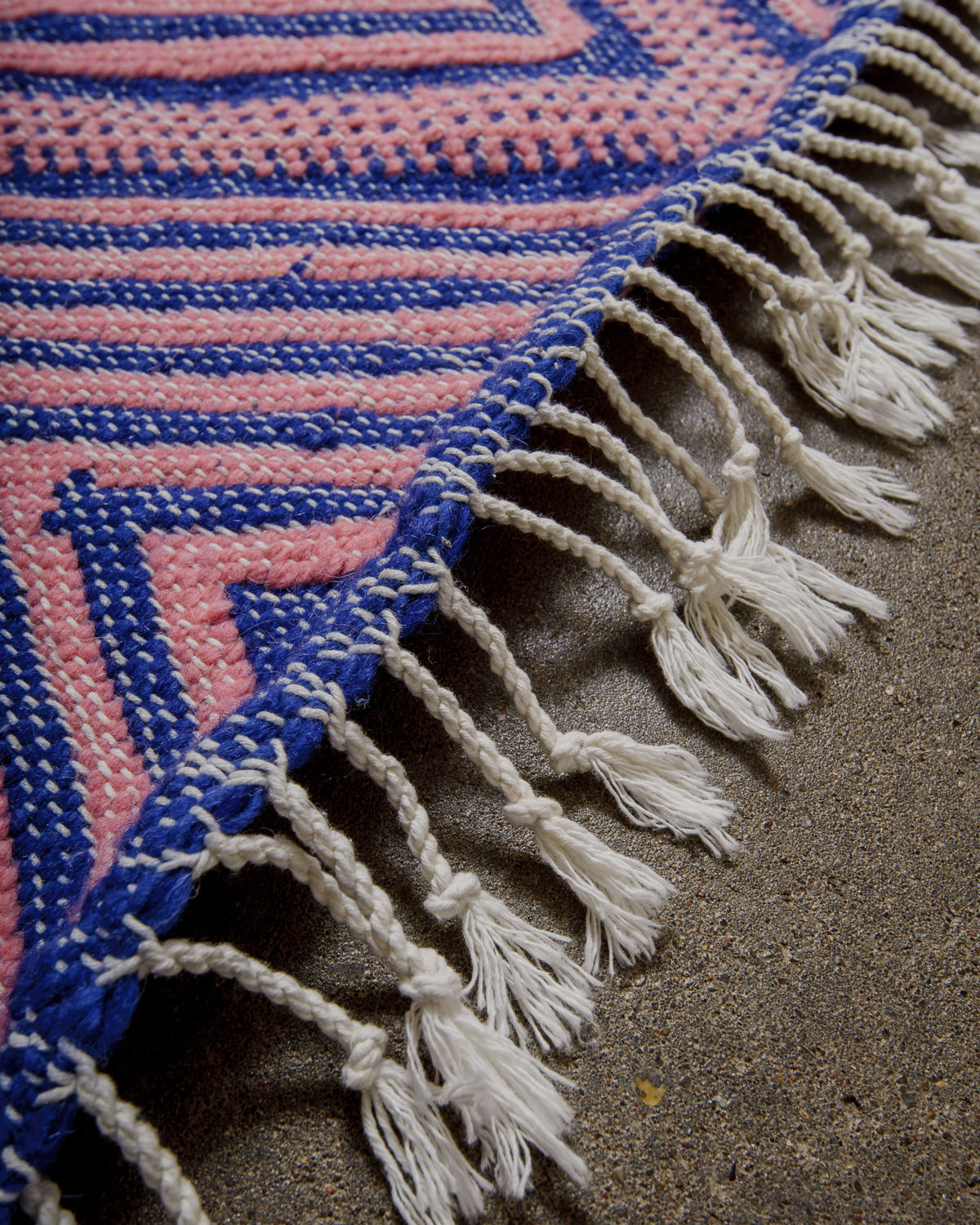 Close-up of a woven rug with pink, blue, and white patterns on cement floor.